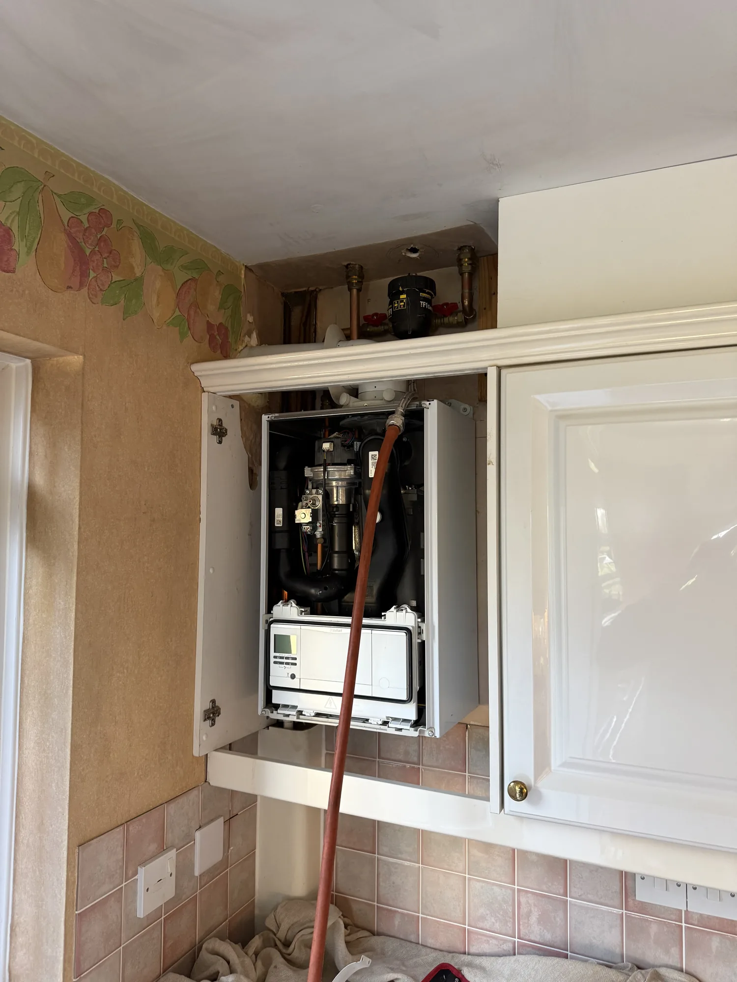 Boiler in a kitchen cupboard with the case off during a repair